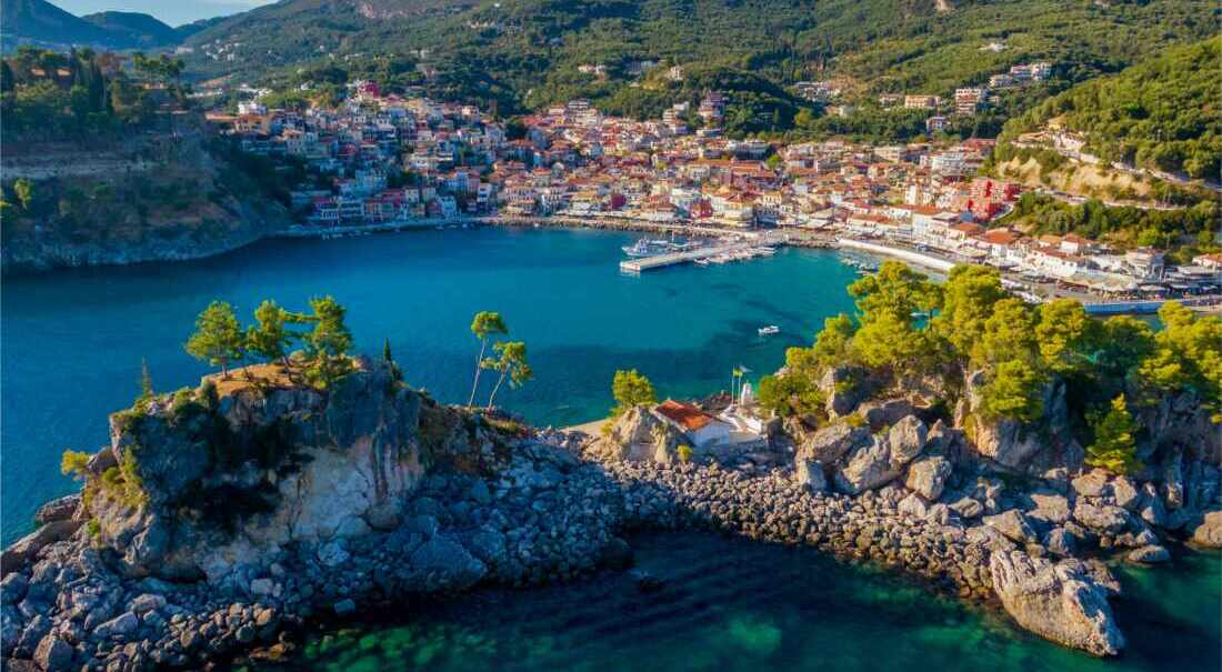 A minimal-chic travel scene with a woman walking along a coastal path in summer neutrals, overlooking the sea and distant islands.